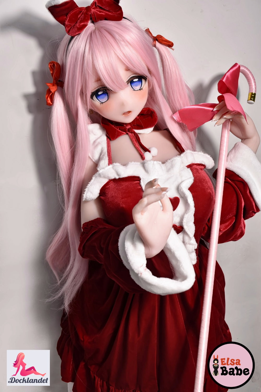 ElsaBabe Itsuki Sango 148 cm anime waifu lėlė, vilki raudoną ir baltą kalėdinę suknelę su lankeliais, rožiniais plaukais ir mėlynomis akimis, laiko rausvą lazdelę su dideliu lankeliu.